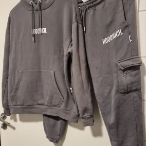 Hoodrich dress st small - Säljer en grå dredd från Hoodrich med tryck både fram och bak. Hoodien har en stor ficka framtill och justerbar huva med snören. Perfekt för en avslappnad stil. Finns en liten dold fläck fram som ej direkt syns el stör funktionen 