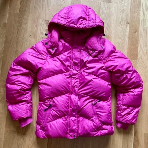 Rosa dunjacka från Nike - Säljer en snygg rosa dunjacka från Nike med huva och dragkedja. Det står storlek M på jackan men den är liten i storleken (jag har storlek S själv). Jackan har långa ärmar och praktiska fickor med dragkedjor. Perfekt för kyliga dagar när du vill hålla dig varm och stilren. 💖