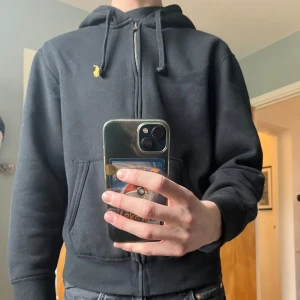 Svart full-zip hoodie Ralph Lauren  - Säljer en fleece svart hoodie från Ralph Lauren med dragkedja i storleken S. En mjuk insida med ett rutigt mönster för huvan. Nypris: 1 895kr. Säljer för att den var lite för liten för mig i storleken (är generellt en M). Knappt använd, begagnad och i mycket gott skick. Här är en länk till hoodiens hemsida: https://www.ralphlauren.eu/se/en/dpid-authenticated?authActionId=VEHFGF4XeSfnV6xFDfcWqEet&webstoreAvailable=true 
