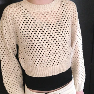Beige stickad tröja från H&M - Säljer en snygg beige stickad tröja från H&M. Tröjan har ett hålmönster och långa ärmar, perfekt för lager-på-lager-stil. Den är croppad och har ribbade muddar vid ärmslut och nederkant. Passar perfekt för en avslappnad look.