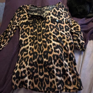 Leopardmönstrad långärmad tröja - Snygg leopardmönstrad tröja med långa ärmar och dekorativa knappar på bröstfickorna. Perfekt för att ge en djärv touch till din outfit. 🐆