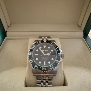 Seiko GMT Sprite - Säljer en stilren Seiko klocka med svart urtavla och en tvåfärgad bezel i svart och grön. Klockan har en robust stållänk och tydliga markeringar på urtavlan. Perfekt för den som söker en kombination av funktion och stil.