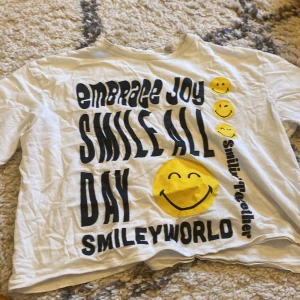Vit t-shirt med smileytryck från H&M - Vit SMILEY WORLD t-shirt från H&M. Storlek 158/164. Säljer då den inte kommer till användning🩷 Kommer strykas innan den skickas🫶🏻💗🌟