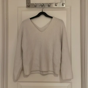 Vit stickad tröja från H&M - Säljer en stilren vit stickad tröja från H&M. Tröjan har en v-ringad design och långa ärmar, perfekt för kyligare dagar. Den är mjuk och bekväm, idealisk för både vardag och avslappnade tillfällen. Storlek S.