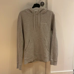 Grå hoodie från J.Lindeberg - Säljer en stilren grå hoodie från J.Lindeberg. Den har en klassisk design  Perfekt för en avslappnad look.Storlek Small