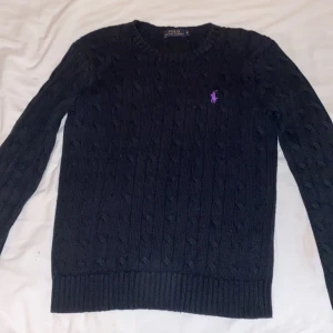 Svart stickad tröja från Ralph Lauren - Säljer en klassisk svart stickad tröja från Ralph Lauren med lila logga på bröstet. Tröjan har en rund halsringning och långa ärmar, perfekt för kyligare dagar. Passar både till vardags och mer uppklädda tillfällen. Passar 158 i barnstorlek alltså ungefär 12-13 åringar!