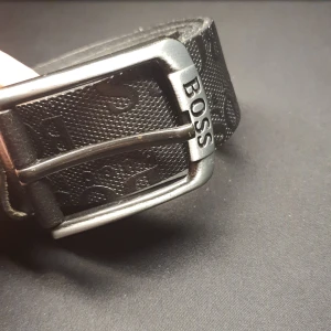 Svart läderbälte från BOSS - Snyggt svart bälte i äkta läder från Boss med präglad logotyp längs remmen. Bältet har ett stilrent silverfärgat spänne med Boss-logga. Perfekt för att ge en elegant touch till din outfit.