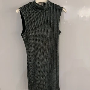  grön ärmlös klänning från Vila - Snygg ärmlös klänning från Vila i olika gröna nyanser och glittriga ränder. Perfekt för en kväll ute eller en speciell tillställning. Klänningen har en hög krage och är i ett stretchigt material som ger en bekväm passform.