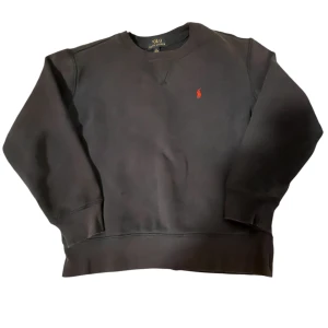 Svart sweatshirt från Ralph Lauren - Säljer en klassisk svart sweatshirt från Ralph Lauren med det ikoniska röda logotypbroderiet på bröstet. Tröjan har långa ärmar och en rund halsringning. Den har två lilla hål och den är äkta. Går att diskutera priset.