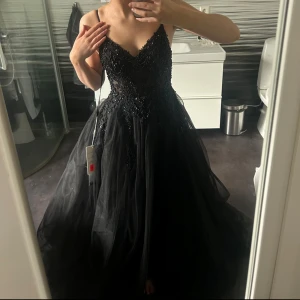 Svart balklänning  - Intressekoll!!Hel ny! Endast testad och köpt på dressroom i Göteborg. Elegant svart balklänning med smala axelband och v-ringad urringning. Klänningen har vackra paljettapplikationer på överdelen och ett flödande kjolparti. Perfekt för en glamorös kväll. Jag är ungefär 160.🫶har inlägg!