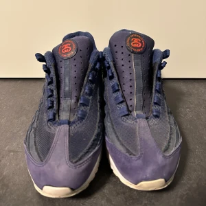 Blå sneakers från Nike x Stussy - Snygga blå sneakers från Nike i samarbete med Stussy. Skorna har en unik design med perforerade detaljer och en vit sula. Perfekta för dig som vill ha något stilrent och bekvämt. Lite små i storlek tyvär inga skosnören 