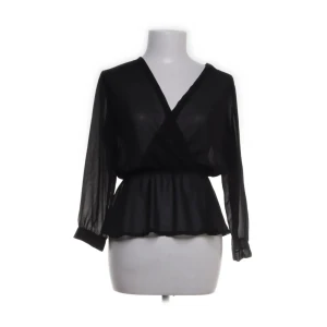 Svart blus med v-ringning - Elegant svart blus med v-ringning och transparenta långa ärmar. Blusen har en omlott-design och en elastisk midja som ger en smickrande passform. Perfekt för en stilren look.