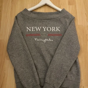 Grå sweatshirt från H&M - Säljer en grå sweatshirt från H&M med texten 'New York Fairytales' tryckt på framsidan. Tröjan har långa ärmar och en bekväm passform. Perfekt för en avslappnad stil.