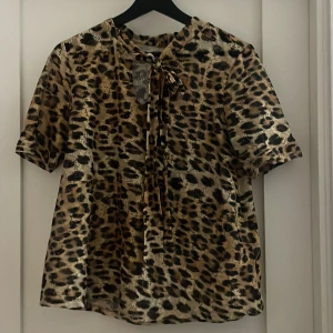 Leopardmönstrad blus från H&M - Snygg leopardmönstrad blus från H&M med korta ärmar och knytband vid halsen. Jätteskönt material. Jag har bara använt den en gång så är i mycket fint skick.