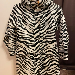 Zebramönstrad regnjacka från Lindberg - Snygg regnkappa från Lindberg i zebramönster. Jackan har en justerbar midja med dragsko. Jackan är i fint skick men kan behöva en tvätt.
