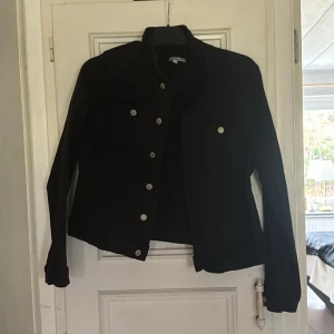 Svart jacka med knappar - Snygg svart jacka med knappar framtill. Perfekt för en stilren look. Jackan har långa ärmar och en klassisk design som passar till många tillfällen.