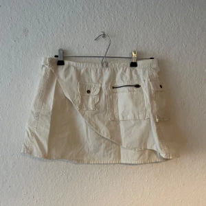 Beige omlottkjol från Marwin - Säljer en snygg vintage vit omlottkjol från Marwin. Kjolen har praktiska fickor med knappar och dragkedja framtill. Perfekt för en avslappnad stil. 👜