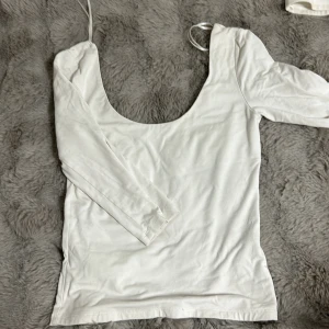 Vit topp från Gina Tricot - Säljer en stilren vit topp från Gina Tricot i storlek S. Toppen har en djup rundad urringning och långa ärmar. Perfekt för en enkel och snygg look.