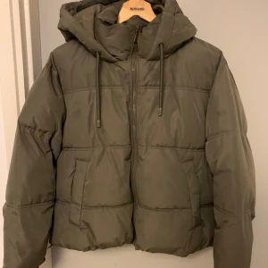 Grön pufferjacka från Zara - Säljer en snygg grön pufferjacka från Zara med huva och dragkedja. Jackan har en quiltad design och är perfekt för kyligare dagar. Den har en normal passform och är tillverkad i ett syntetmaterial.