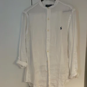 Vit skjorta från Ralph Lauren - Säljer en stilren vit skjorta från Ralph Lauren i slim fit. Skjortan har långa ärmar och knappar framtill. Den är tillverkad i ett lätt och bekvämt material med en broderad logotyp på bröstet. Perfekt för en elegant look, linne material. Äkta, storlek S. 