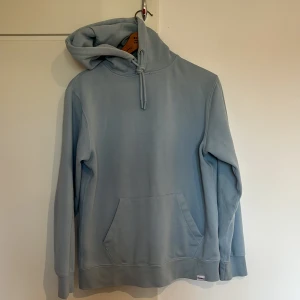 Ljusblå hoodie från Pull&Bear - Säljer en stilren ljusblå hoodie från Pull&Bear. Den har en klassisk design med en stor ficka framtill och justerbar huva. Perfekt för en avslappnad look. 🌀