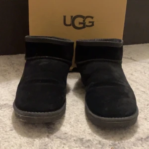 Uggs - Säljer ett par svarta boots från UGG i mjukt material. De har en klassisk design med rund tå och låg profil, perfekt för kyligare dagar.