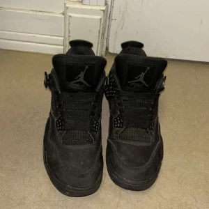 Jordans 4 - Säljer ett par svarta Nike Air Jordans med klassisk design och snörning. Skorna har en stilren look med detaljer i syntetmaterial och en bekväm passform.