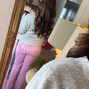 Rosa mjukisbyxor från Juicy Couture - Säljer ett par rosa mjukisbyxor från Juicy Couture med glittrig text på baksidan. Byxorna har en bekväm passform och är perfekta för en avslappnad stil. De är tillverkade i ett mjukt material som känns skönt mot huden.