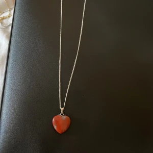 Halsband med rött hjärthänge - Elegant halsband med ett rött hjärthänge. Kedjan är tunn och silverfärgad, vilket ger en fin kontrast till det röda hjärtat. Perfekt för att ge en färgklick till din outfit.