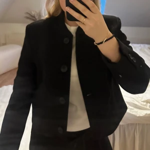 Svart kavaj från Zara - Snygg svart kavaj från Zara med knappar framtill i ull. Perfekt för en stilren look. Kavajen har en klassisk design med långa ärmar och en rak passform. Använd 1 gång i storlek S