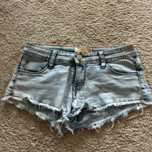 Lågmidjade shorts - Säljer ett par ljusblå jeansshorts från Miss RJ med fransiga kanter och klassisk femficksdesign. Perfekta för en avslappnad stil. De har en knapp och dragkedja framtill. Storlek 38 men små så passar S