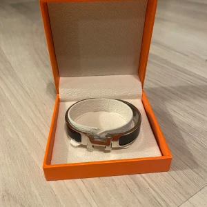Svart armband  - Elegant svart armband med silverdetaljer. Armbandet kommer i en lyxig orange förpackning. Perfekt accessoar för att lyfta vilken outfit som helst.
