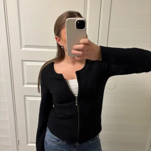 Svart stickad kofta med dragkedja - Snygg svart stickad kofta med dragkedja framtill. Perfekt för kyligare dagar och enkel att matcha med olika outfits. Koftan har långa ärmar och en figurnära passform.