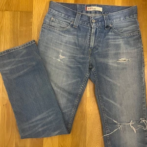 Blå jeans från Levi's 511 - Snygga blå Levi's 511 jeans med slitna detaljer och en slim passform. De har klassisk femficksdesign och knappgylf. Vanligtvis har jag storlek 29 på jeans, dessa är i storlek 31/32 så de är små i storleken kan tänka mig att de passar någon med storlek 28.              Midjemått 80 cm.                                          Pris kan diskuteras. 