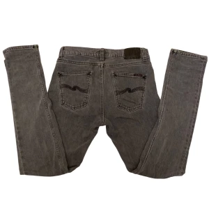 Grå Nudie jeans - Snygga grå jeans från Nudie Jeans med klassisk femficksdesign och subtila broderade detaljer på bakfickorna. Perfekt för en stilren look med en bekväm passform. Modellen är Lean Dean och de är i storleken W28 L32. Kom gärna med prisförslag eller frågor😇🩶