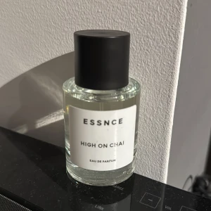 Essnce High on Chai Eau de Parfum - Säljer en flaska Essnce High on Chai Eau de Parfum. Den har en stilren och minimalistisk design med en genomskinlig glasflaska och svart lock. Perfekt för dig som älskar doften av chai och vill ha något unikt i din parfymkollektion. Flaskan är i gott skick och redo att användas. Passa på att köpa denna doftupplevelse!