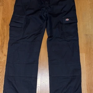 Svarta cargobyxor från Dickies - Säljer ett par svarta cargobyxor från Dickies i bra skick. De har flera praktiska fickor och är perfekta för vardagsbruk eller arbete. Byxorna är tillverkade i slitstarkt material och har en loose passform för extra komfort. Perfekta för höst och vår! Köparen står för frakt!   Casper
