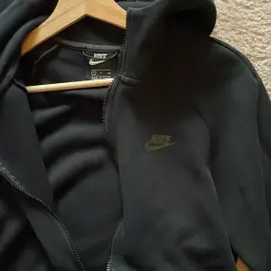 Säljer en svart hoodie från Nike i  bra skick. First Season drop från 2019. Klassiska Nike tech. Den har en dragkedja framtill och en praktisk huva. Perfekt för att sätta ihop en dress eller använda som singel. Passar både till träning och vardagsbruk. Storlek S