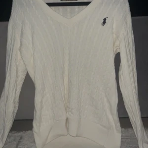 Vit kabelstickad tröja från Ralph Lauren - Säljer en klassisk vit kabelstickad tröja från Ralph Lauren inte äkta! Den har en snygg v-ringning och det ikoniska logotypbroderiet på bröstet. Tröjan är i 100% bomull och perfekt för både höst och vinter. Den är i mycket bra skick och passar perfekt för en stilren look.