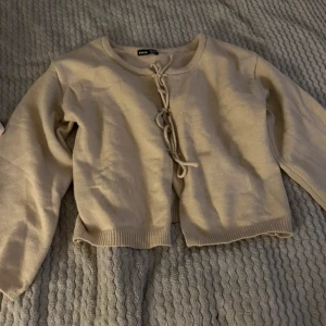 Beige kofta med knytning - Säljer en superfin beige kofta. Den har en söt knytning framtill och är perfekt för både vår och höst. Koftan är i ett mjukt material och har långa ärmar. Passar perfekt till en casual outfit eller för att klä upp en enkel look