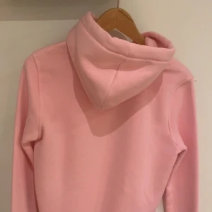 Rosa hoodie från Kenzo - Säljer en snygg rosa hoodie i storleken M men känns som S från Kenzo med broderad logga på framsidan. Tröjan har en stor ficka framtill och justerbar huva med snören. Perfekt för en avslappnad stil!