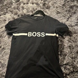 Svart t-shirt från Boss - Säljer en snygg svart t-shirt från Boss med vit text och linjer över bröstet. skicket är 8,5/10. Storlek M. Pris 149kr, om du har bud, frågor eller bilder bara skriva(: