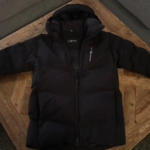 Sail Racing jacka patrol down - Säljer nu en svart Sail Racing patrol down jacka med huva pågrund av att jag har växt ur den och har skaffat en ny. Jackan är perfekt för kalla dagar nu i vinter. Den är i perfekt skick med inga defekter då den användes fåtal gånger och var ganska tight på mig.