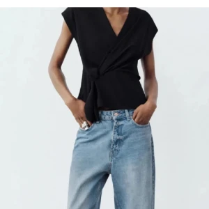 Svart omlottopp - Snygg svart omlottopp med knytning i midjan. Den är ärmlös och har en stilren design som passar perfekt för både vardag och fest. St xs 