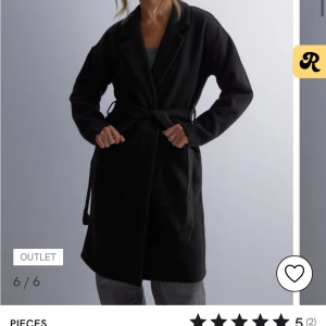 Svart kappa från Pieces - Snygg svart kappa från Pieces, köptes för 550 och är nu slutsåld, som ny då den knappt är använd. Den har ett bälte i midjan för en figursydd look och är perfekt för både höst, vår och vinter. 