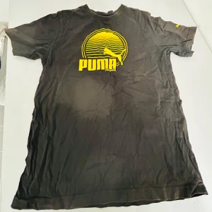 Svart t-shirt från Puma med gult tryck - Säljer en svart t-shirt från Puma i bra skick. Den har ett coolt gult tryck med Puma-loggan på bröstet och en liten logga på ärmen. Perfekt för vardagsbruk eller träning. Materialet känns mjukt och bekvämt. Passar bra till jeans eller shorts!