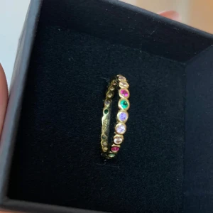 Silver ring - Säljer en superfin guldfärgad ring med små, färgglada stenar runt hela bandet. Perfekt för att ge lite extra färg och glans till din outfit. Ringen är i nytt skick och kommer i en snygg svart ask. Passar perfekt för både vardag och fest!