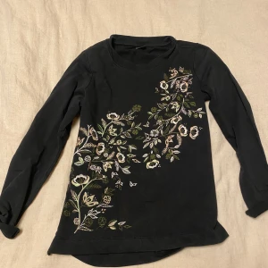 Svart långärmad topp från Gina Tricot - Säljer en svart långärmad topp från Gina Tricot i storlek S. Den har ett vackert blommigt broderi i olika färger på framsidan. Perfekt för höst och vår, och ger en stilren touch till din outfit. Toppen är i bra skick och redo för nya äventyr!