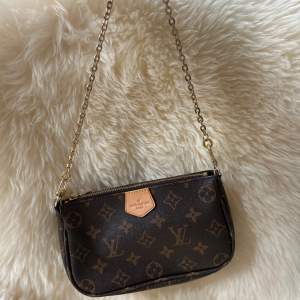 Säljer en snygg brun axelväska från Louis Vuitton med det klassiska monogrammönstret. Väskan har en guldfärgad kedja och en dragkedja upptill. Perfekt för både vardag och fest! 👜✨