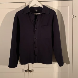 Mörkblå overshirt/cardigan  från Uniqlo - Säljer en stilren mörkblå kofta från Uniqlo med knappar framtill och en bröstficka. Perfekt som overshirt eller bara som kofta.